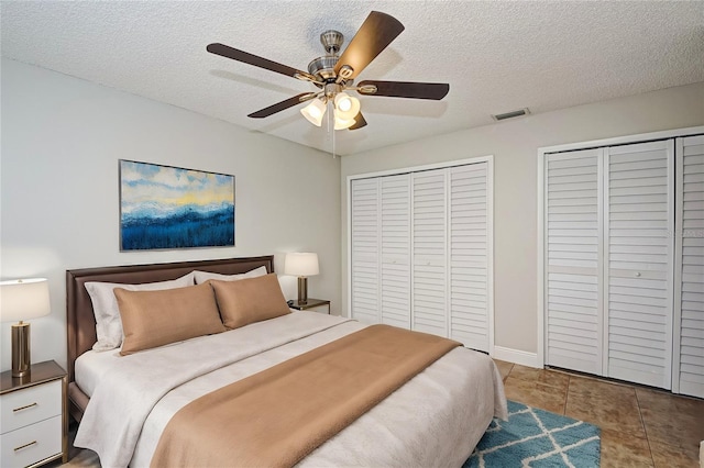 tiled bedroom featuring ceiling fan, a textured ceiling, and two closets