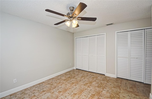 unfurnished bedroom with ceiling fan, light tile patterned floors, a textured ceiling, and two closets