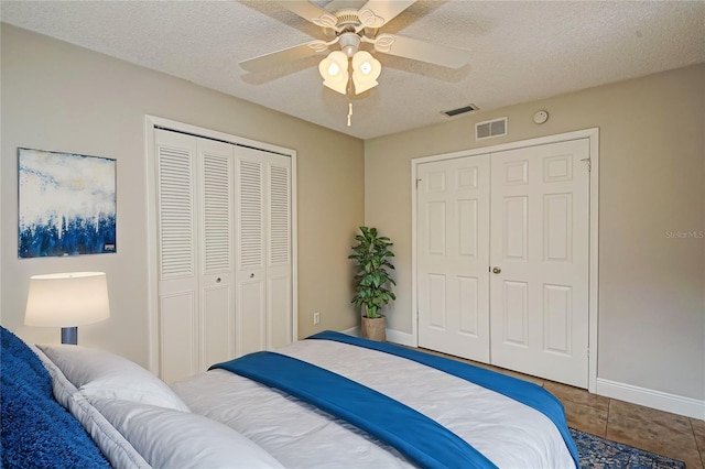 bedroom with a textured ceiling, tile patterned floors, ceiling fan, and multiple closets