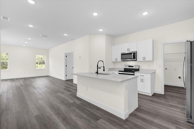 kitchen with appliances with stainless steel finishes, dark hardwood / wood-style flooring, white cabinets, and a kitchen island with sink