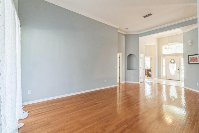 unfurnished living room with light hardwood / wood-style floors, a towering ceiling, and crown molding