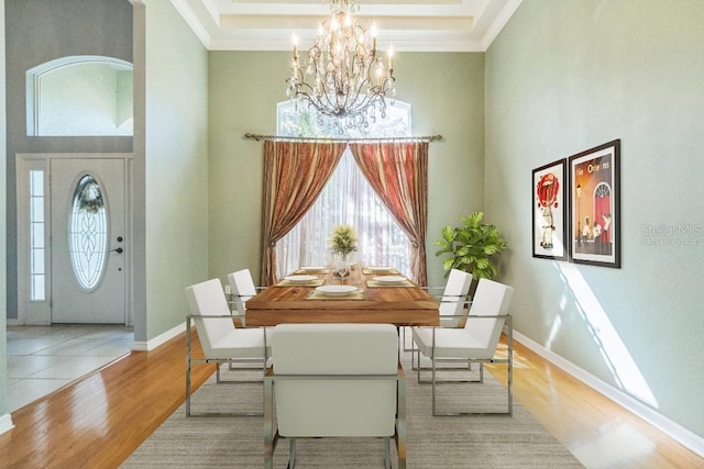 dining room featuring a chandelier, a towering ceiling, light wood-type flooring, and ornamental molding