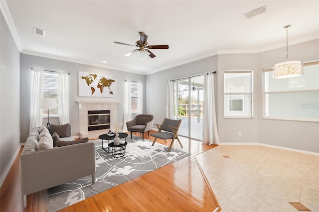 living room featuring ceiling fan, light wood-type flooring, crown molding, and a tiled fireplace