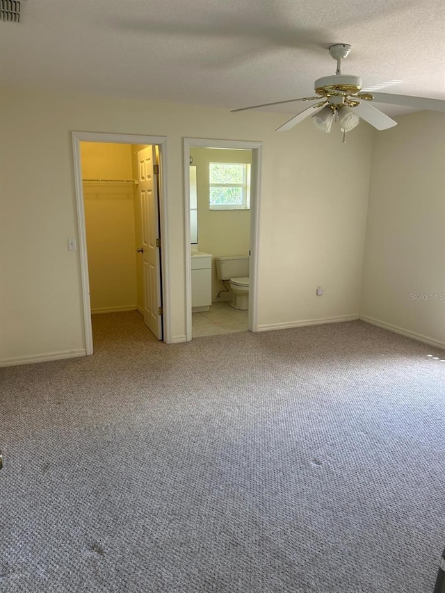 unfurnished bedroom with a closet, light carpet, a walk in closet, ensuite bath, and ceiling fan