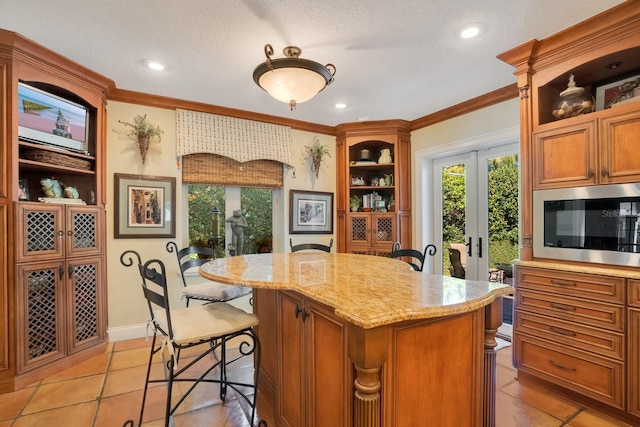 kitchen with light tile patterned floors, a kitchen island, crown molding, french doors, and light stone counters