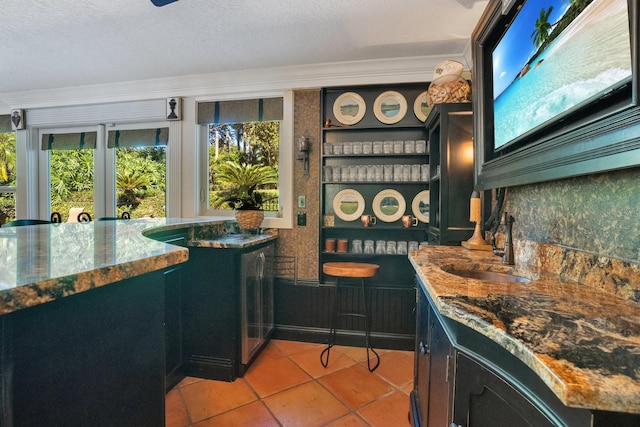 bar featuring stone counters, sink, a textured ceiling, ornamental molding, and light tile patterned floors