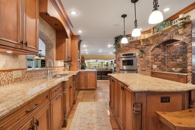 kitchen featuring sink, a kitchen island, double oven, pendant lighting, and light stone counters