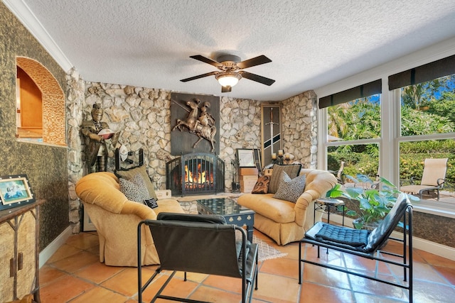 tiled living room featuring a stone fireplace, a textured ceiling, and ceiling fan