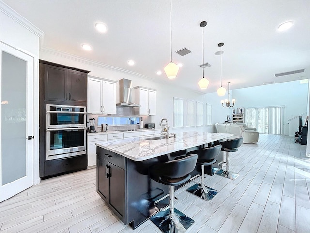 kitchen featuring wall chimney exhaust hood, a kitchen breakfast bar, sink, plenty of natural light, and white cabinets