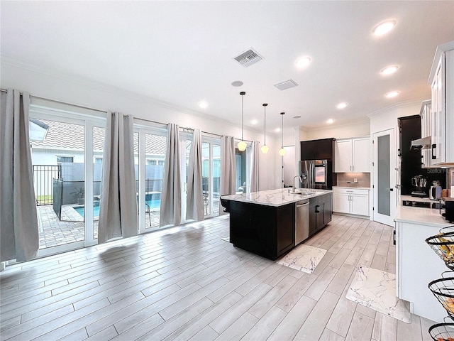 kitchen with an island with sink, stainless steel appliances, sink, white cabinetry, and light hardwood / wood-style floors