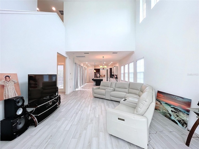 living room featuring an inviting chandelier, light hardwood / wood-style floors, and a towering ceiling