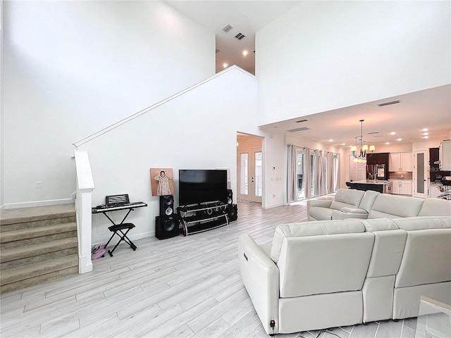 living room with light hardwood / wood-style floors, a high ceiling, and an inviting chandelier