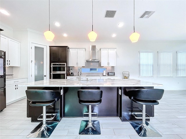 kitchen with a large island, a breakfast bar area, sink, wall chimney exhaust hood, and decorative light fixtures