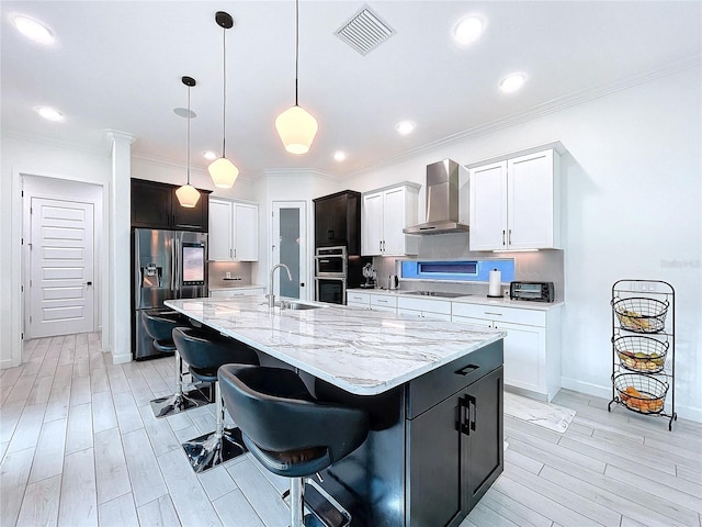 kitchen featuring wall chimney range hood, a kitchen bar, hanging light fixtures, stainless steel appliances, and a kitchen island with sink