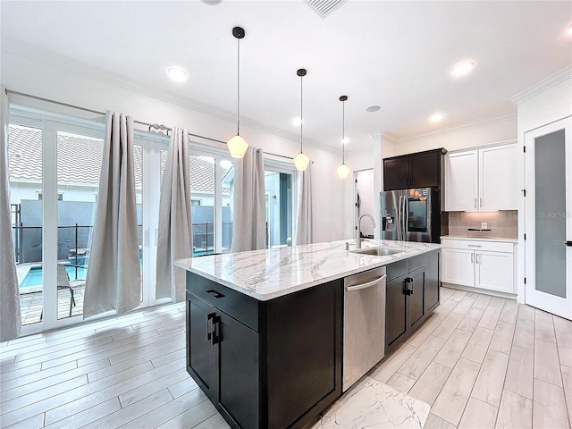 kitchen with an island with sink, sink, decorative light fixtures, white cabinetry, and appliances with stainless steel finishes