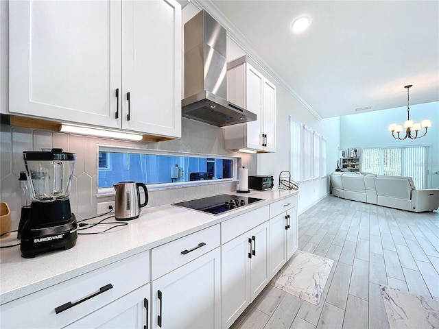 kitchen with a notable chandelier, wall chimney range hood, black electric cooktop, and white cabinets