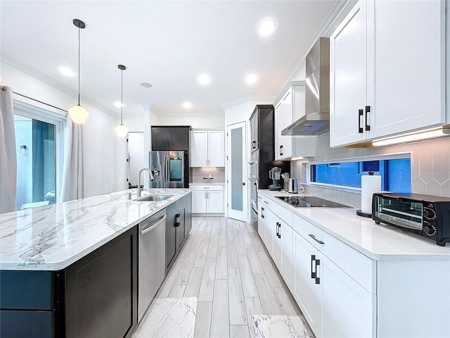 kitchen featuring wall chimney range hood, hanging light fixtures, sink, white cabinets, and appliances with stainless steel finishes