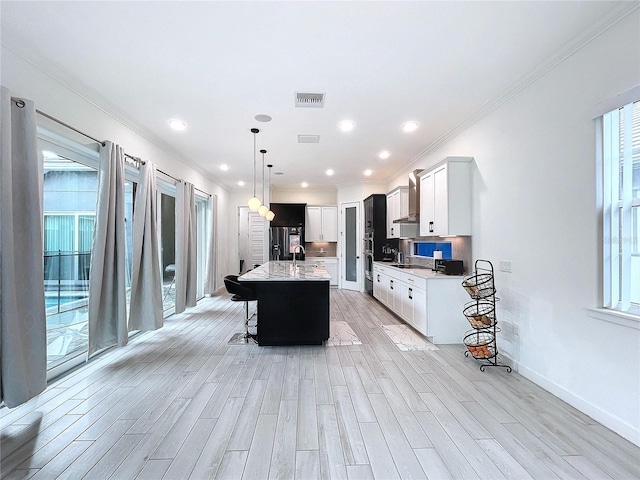 kitchen with light wood-type flooring, decorative light fixtures, white cabinets, a breakfast bar, and a center island with sink