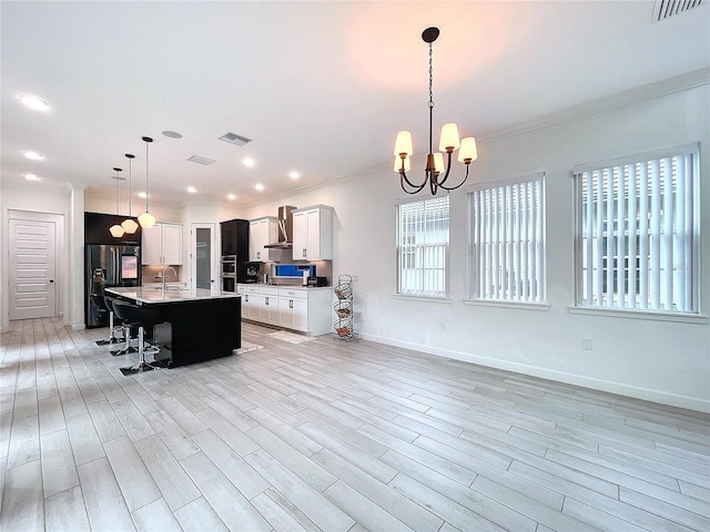 kitchen with a breakfast bar, white cabinets, decorative light fixtures, and a center island with sink