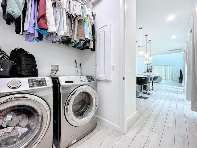 laundry area featuring independent washer and dryer, electric panel, light wood-type flooring, and an inviting chandelier