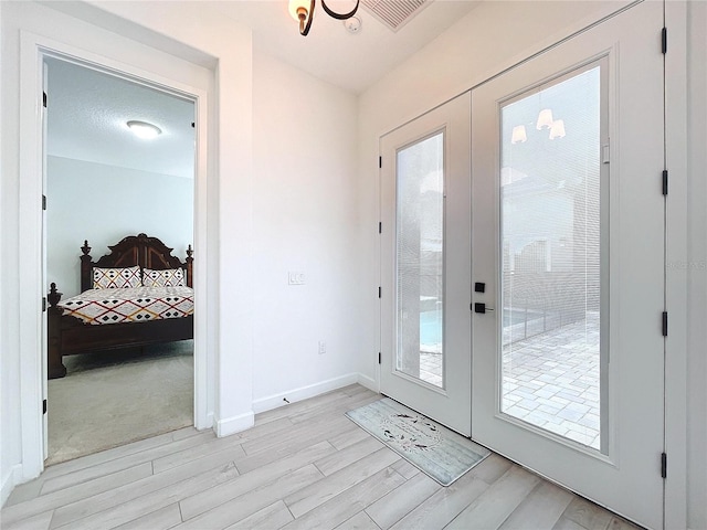 doorway featuring light hardwood / wood-style floors, french doors, a textured ceiling, and a healthy amount of sunlight