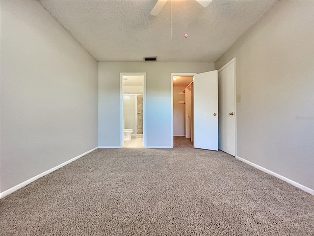 unfurnished bedroom with carpet, a walk in closet, a textured ceiling, ceiling fan, and connected bathroom