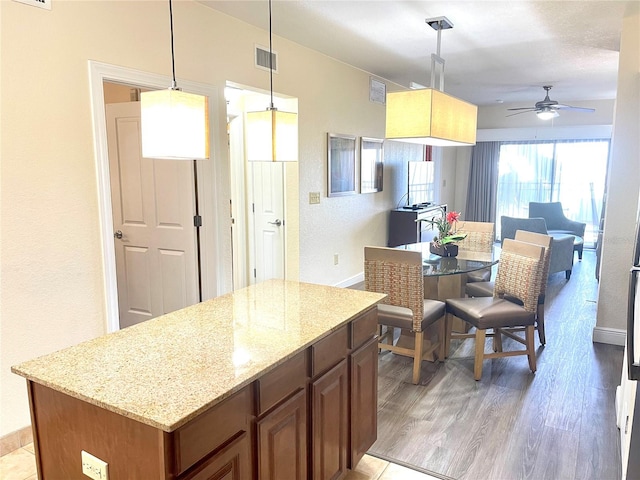 kitchen featuring ceiling fan, light stone countertops, pendant lighting, light hardwood / wood-style floors, and a center island