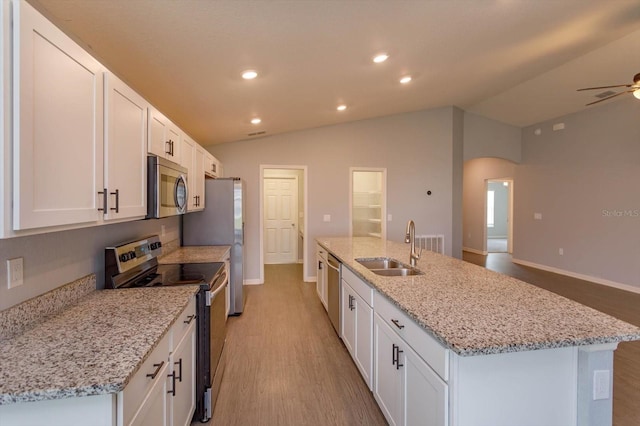 kitchen with light stone countertops, an island with sink, white cabinetry, stainless steel appliances, and lofted ceiling