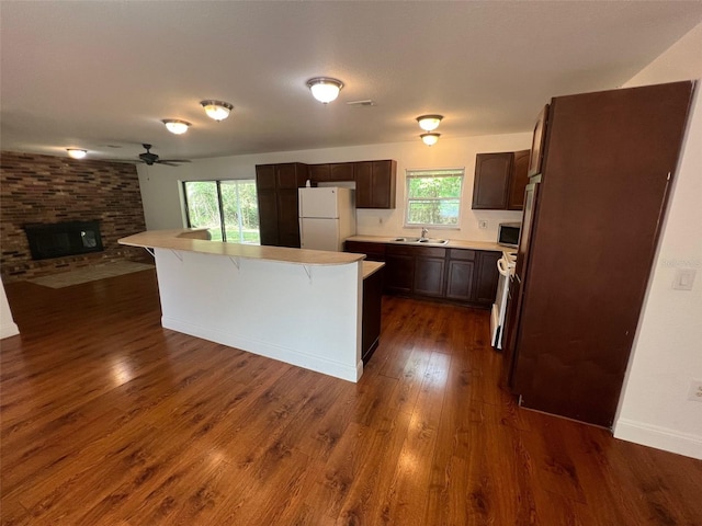 kitchen featuring dark wood-type flooring, a brick fireplace, white refrigerator, and a kitchen island