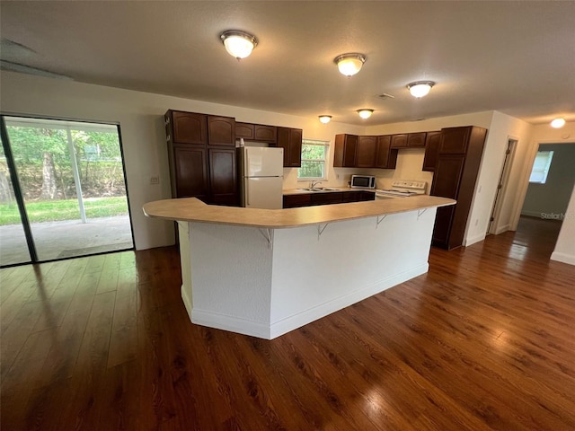 kitchen featuring dark hardwood / wood-style floors, sink, a center island, dark brown cabinetry, and white appliances