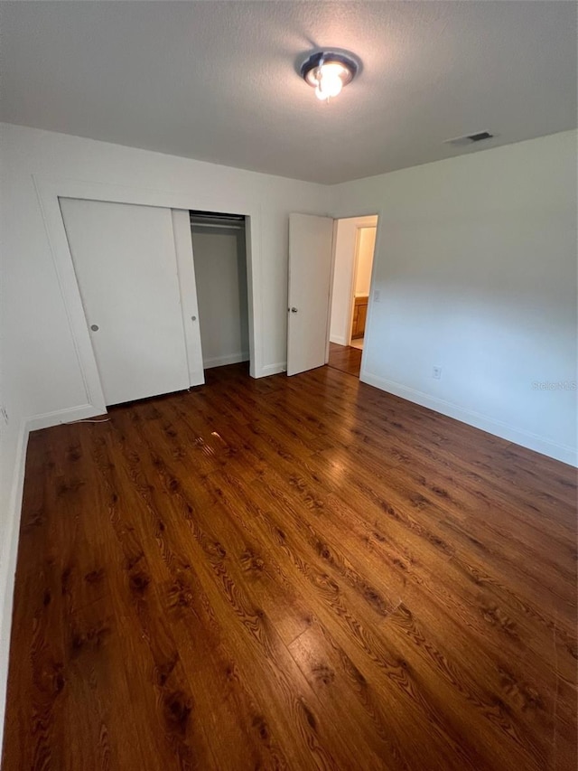 unfurnished bedroom featuring a textured ceiling, dark hardwood / wood-style floors, and a closet