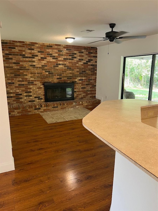 unfurnished living room with dark wood-type flooring, a brick fireplace, and ceiling fan