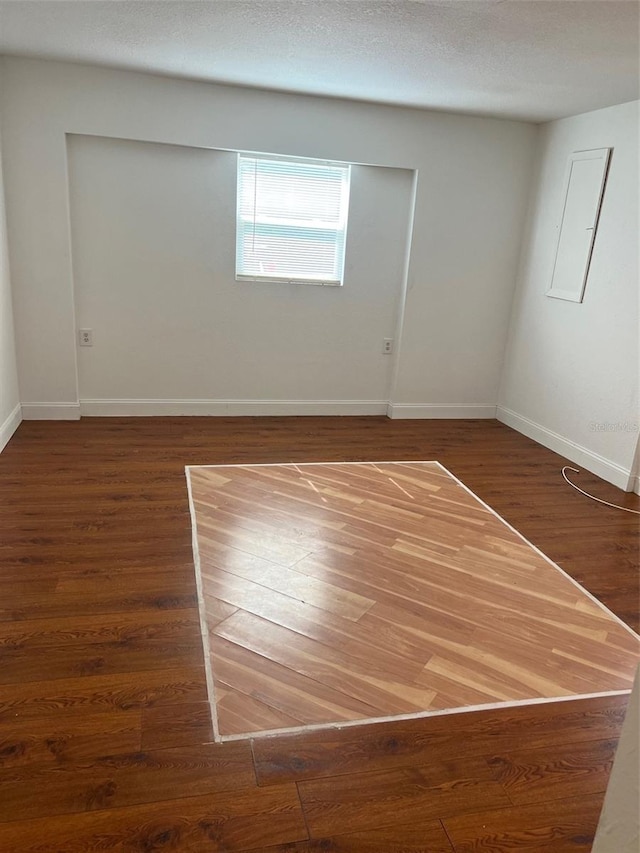 empty room featuring electric panel, a textured ceiling, and dark hardwood / wood-style flooring