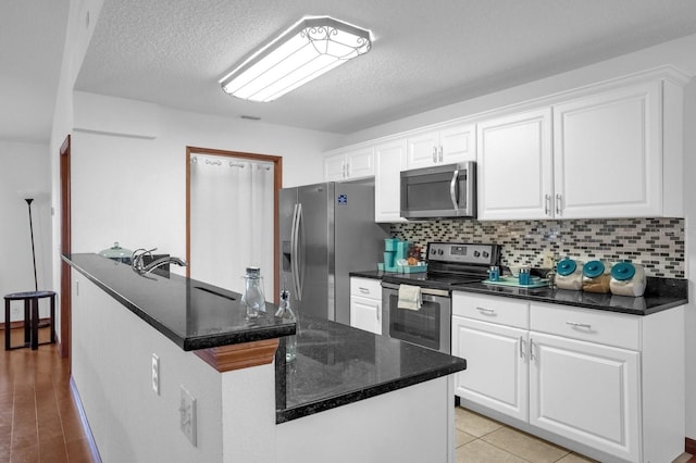 kitchen with backsplash, appliances with stainless steel finishes, white cabinetry, a textured ceiling, and light hardwood / wood-style flooring