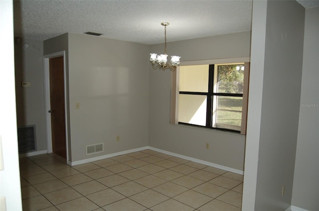 tiled spare room featuring a notable chandelier and a textured ceiling