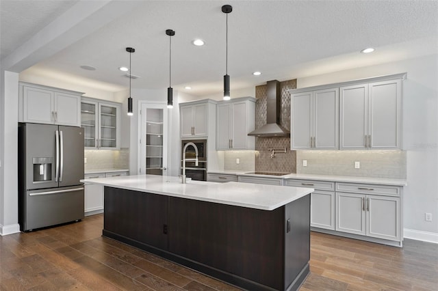 kitchen with a kitchen island with sink, hanging light fixtures, black electric stovetop, stainless steel fridge with ice dispenser, and wall chimney exhaust hood