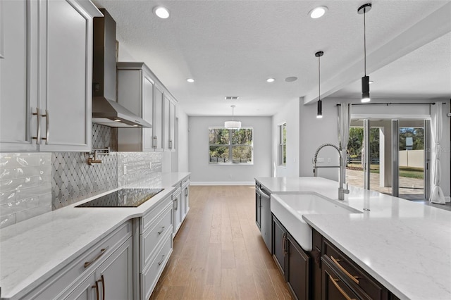 kitchen featuring decorative light fixtures, decorative backsplash, light stone countertops, and wall chimney exhaust hood