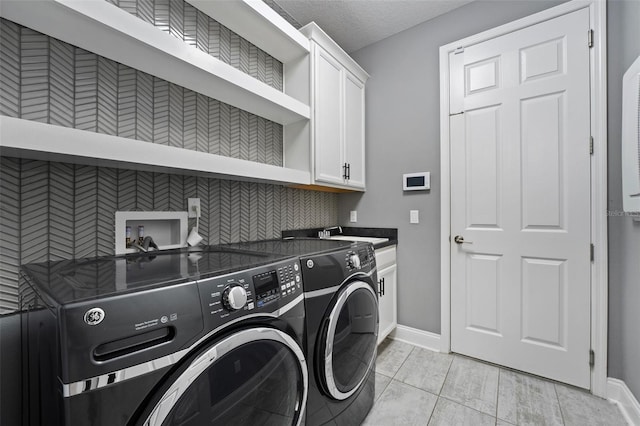 clothes washing area with sink, cabinets, a textured ceiling, light tile patterned flooring, and separate washer and dryer