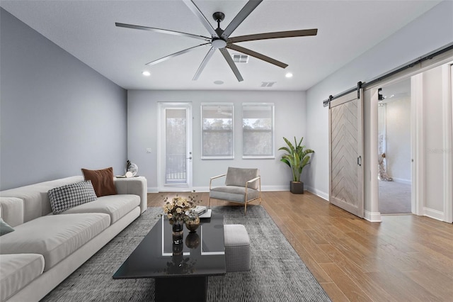 living room featuring light hardwood / wood-style flooring, a barn door, and ceiling fan