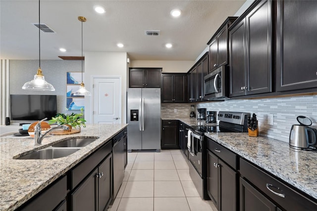 kitchen with appliances with stainless steel finishes, sink, dark brown cabinets, decorative light fixtures, and light stone counters