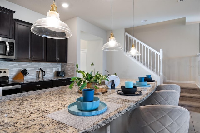 kitchen featuring appliances with stainless steel finishes, light stone countertops, decorative light fixtures, and backsplash