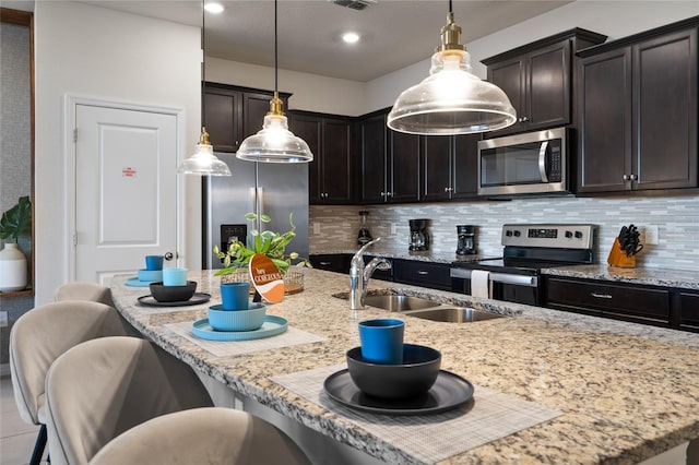 kitchen featuring sink, appliances with stainless steel finishes, a breakfast bar area, and decorative light fixtures