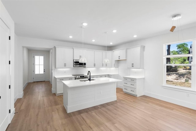 kitchen with an island with sink, white cabinetry, light hardwood / wood-style floors, decorative light fixtures, and stainless steel appliances