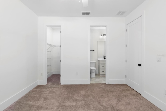 unfurnished bedroom with a closet, a walk in closet, ensuite bath, light colored carpet, and ceiling fan