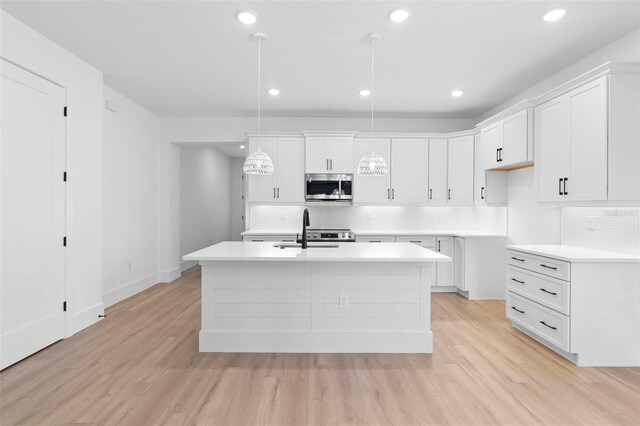 4190 Rossmore Dr, Orlando, FL 32810 - kitchen featuring stainless steel microwave, a sink, an island with sink, backsplash, and light wood finished floors