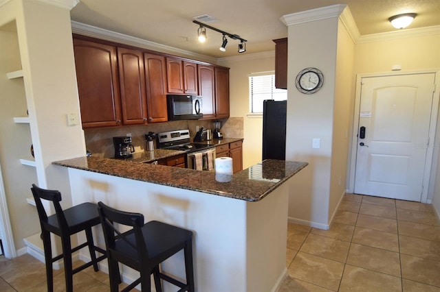 kitchen with decorative backsplash, kitchen peninsula, dark stone counters, black appliances, and a breakfast bar