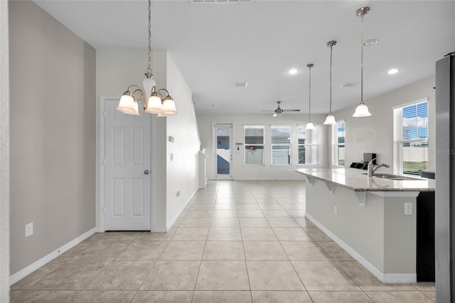 kitchen with a breakfast bar, sink, light tile patterned flooring, hanging light fixtures, and light stone countertops