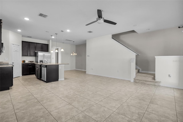 kitchen with ceiling fan, hanging light fixtures, stainless steel appliances, light stone counters, and a center island with sink