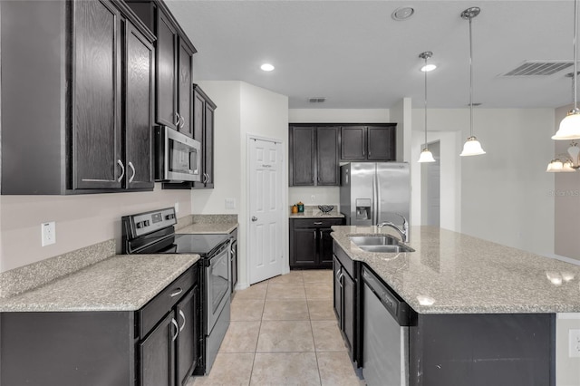 kitchen with appliances with stainless steel finishes, an island with sink, decorative light fixtures, light tile patterned floors, and sink