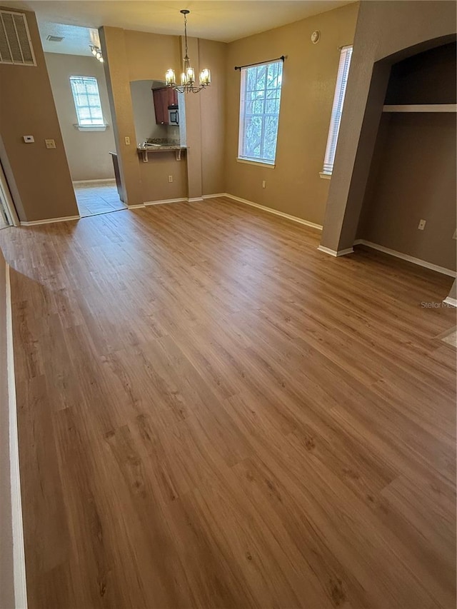 unfurnished dining area with a notable chandelier, a wealth of natural light, and light wood-type flooring